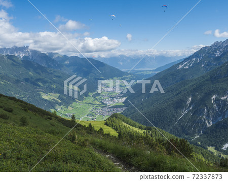 View over green Stubai valley and Neustift im Stubaital village from Elferhutte with moutain peaks and kites. Tirol Alps, Austria, Summer blue sky, white clouds 72337873