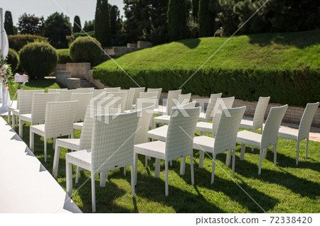Beautiful outgoing wedding set up.Romantic wedding ceremony , wedding outdoor on the lawn water view. Wedding decor. White wooden chairs on a green lawn. White armchairs for guests 72338420