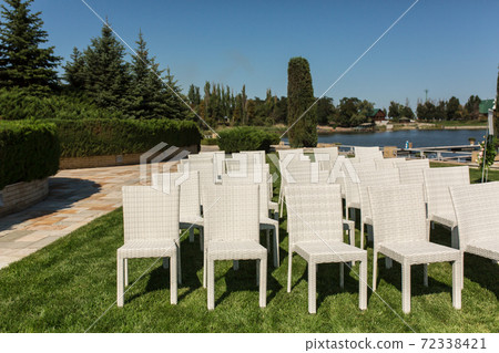 Beautiful outgoing wedding set up.Romantic wedding ceremony , wedding outdoor on the lawn water view. Wedding decor. White wooden chairs on a green lawn. White armchairs for guests 72338421