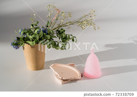 pink menstrual cup with flowers on white background with sunlight and shadows pink menstrual cup with flowers on white background with sunlight and shadows 72338709