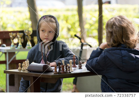 Smart Girl, seven years old is taking part a kids chess tournament outdoor in the park. Smart Girl, seven years old is taking part a kids chess tournament outdoor in the park. 72338757