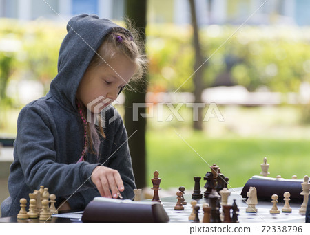 Smart Girl, seven years old is taking part a kids chess tournament outdoor in the park. Smart Girl, seven years old is taking part a kids chess tournament outdoor in the park. 72338796