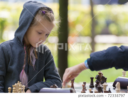 Smart Girl, seven years old is taking part a kids chess tournament outdoor in the park. 72338797