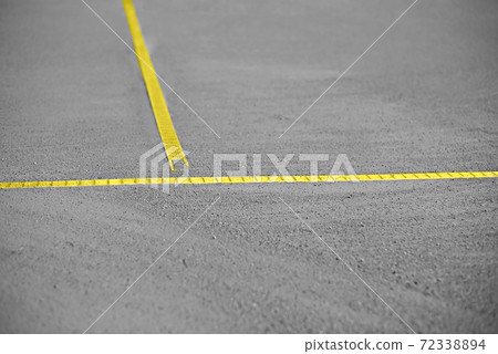 Gray sand and gravel base of the tennis court with yellow lines. 72338894