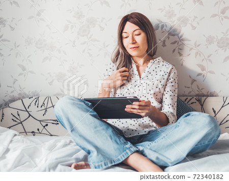 Woman sits on bed with tablet PC. She watches online TV series. Online video call or conference, distance learning, remote education. Self isolation during quarantine. Woman sits on bed with tablet PC. She watches online TV series. Online video call or conference, distance learning, remote education. Self isolation during quarantine. 72340182
