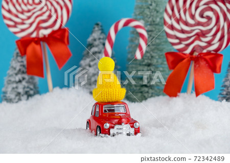 Red Santa car with in yellow winter cap and Christmas tree forest with candies and lollipops sweets. Merry Christmas and Happy New Year Red Santa car with in yellow winter cap and Christmas tree forest with candies and lollipops sweets. Merry Christmas and Happy New Year 72342489