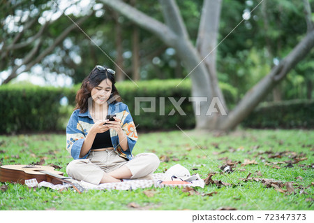 Beautiful Asian student picnic in the park and thinking Composing song 72347373