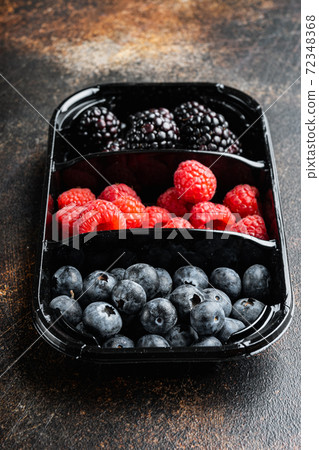 Fresh berries are packed in tray, blueberries, raspberry and blackberry, on old dark table Fresh berries are packed in tray, blueberries, raspberry and blackberry, on old dark table 72348368
