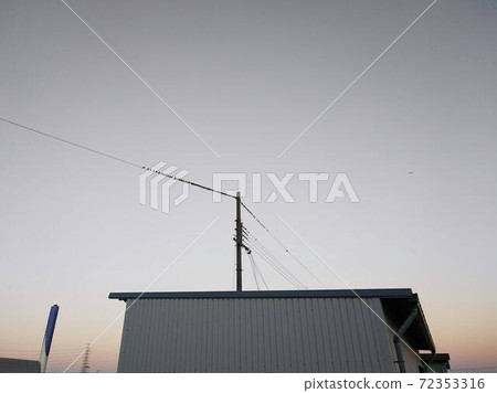 在暮色中，東方的天空被染成粉紅色的灰色。一群鳥停在農場棚子上的電線上 72353316