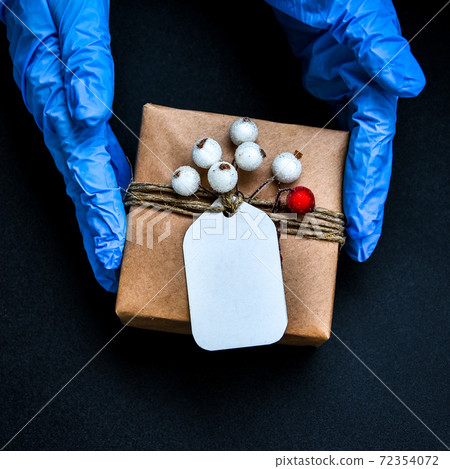 Holiday shopping. Festive gifts. Pandemic restriction. Winter shopping. Hand in protective gloves holding present zero waste box. Advertising background. Pandemic. Stay safe. Holiday shopping. Festive gifts. Pandemic restriction. Winter shopping. Hand in protective gloves holding present zero waste box. Advertising background. Pandemic. Stay safe. 72354072