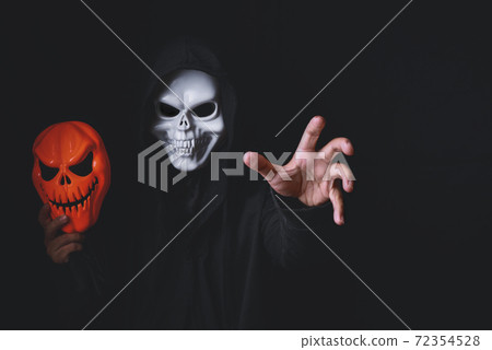 Horror devil costume with spooky pumpkin skull in black dressed for halloween carnival. Devil cosplay holding ghost mask and raise hand with blank copy space for your advertising content. 72354528