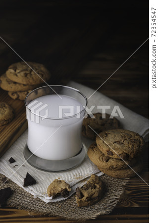 Glass of milk with appetizing delicious sweet homemade chocolate chip on dark vintage wooden table. Tasty dessert for breakfast with copy space for your advertising content Glass of milk with appetizing delicious sweet homemade chocolate chip on dark vintage wooden table. Tasty dessert for breakfast with copy space for your advertising content 72354547