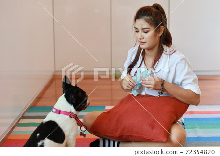 beautiful young asian woman wearing white shirt and holding red pillow who sitting and playing with her cute dog with happy and smiling face in living room. (lifestyle concept) 72354820