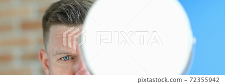 Young man with remnants of hair paste on head stands with mirror in hands portrait 72355942
