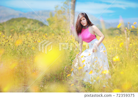 Asian beautiful woman, long hair in pink dress on yellow cosmos filed in winter with blue sky and mountain. Beautiful cute girl portrait with flowers in background. Travel in nature outdoor concept 72359375