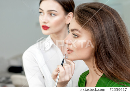 Makeup artist applies lipstick. 72359617