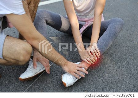 young man helping jogger woman who wearing sport suit and hurt the ankle from too much exercise in the park young man helping jogger woman who wearing sport suit and hurt the ankle from too much exercise in the park 72359701