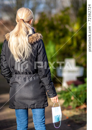 Woman, standing at the grave of family members with a facemask during the pandemic Woman, standing at the grave of family members with a facemask during the pandemic 72362724