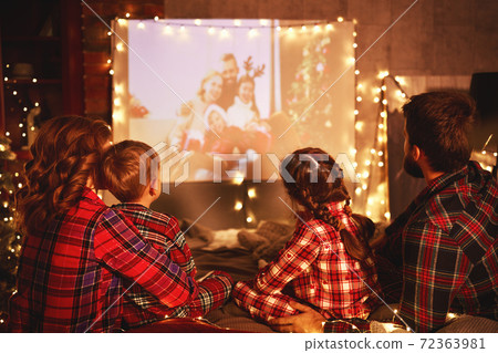 family mother father and children watching projector, film, movies with popcorn in   christmas evening   at home. 72363981