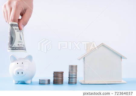 Hand putting money paper into piggy bank with wooden house and stack coins isolated grey background. Property investment and house mortgage financial concept. 72364037