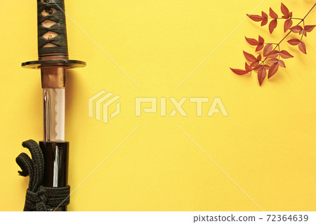 A bare Japanese sword placed on the left edge of a yellow paper background and a red leaf tree branch placed on the right edge. Copy space in the center. 72364639