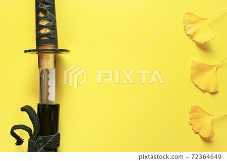 A bare Japanese sword placed on the left edge of a yellow paper background and three ginkgo leaves placed on the right edge. Copy space in the center. A bare Japanese sword placed on the left edge of a yellow paper background and three ginkgo leaves placed on the right edge. Copy space in the center. 72364649
