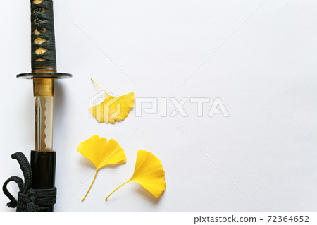 A Japanese sword and three yellow ginkgo leaves placed on the left side of a white paper background. Copy space on the right. A Japanese sword and three yellow ginkgo leaves placed on the left side of a white paper background. Copy space on the right. 72364652