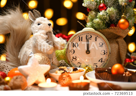 christmas or holiday decoration background - small fir tree, retro alarm clock shows midnight and sweet food. New year still life with xmas lights christmas or holiday decoration background - small fir tree, retro alarm clock shows midnight and sweet food. New year still life with xmas lights 72369513