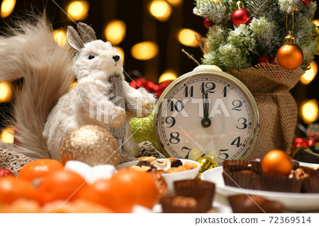 christmas or holiday decoration background - small fir tree, retro alarm clock shows midnight and sweet food. New year still life with xmas lights 72369514