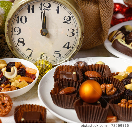 sweet food background for christmas or holiday decoration - chocolate candies, tangerines, nuts and dried fruits on white wood 72369516
