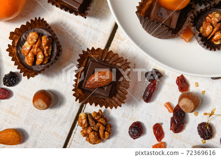 sweet food background for christmas or holiday decoration - chocolate candies, tangerines, nuts and dried fruits on white wood 72369616