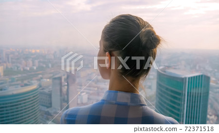 Back view of woman looking at cityscape through window of skyscraper Back view of woman looking at cityscape through window of skyscraper 72371518