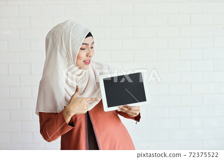 young muslim businesswoman showing blank tablet screen and pointing it (you can put letter on it) young muslim businesswoman showing blank tablet screen and pointing it (you can put letter on it) 72375522