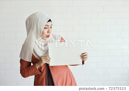 young muslim businesswoman showing blank white paper and pointing it (you can put letter on it) 72375523