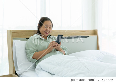 Happy senior woman enjoying using mobile apps texting typing messages sit on bed. 72378226