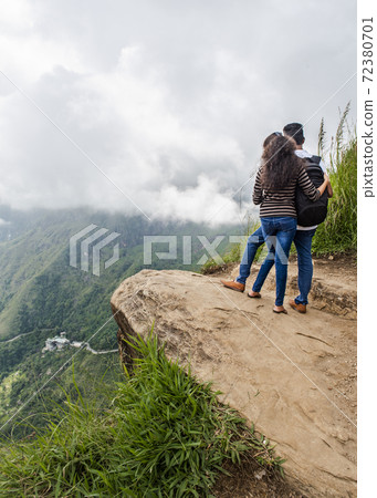A couple of young people on the edge of a mountain cliff admiring valley on the island of Sri Lanka A couple of young people on the edge of a mountain cliff admiring valley on the island of Sri Lanka 72380701