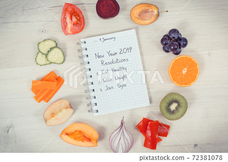 Ripe fruits and vegetables, new year resolutions written in notepad 72381078