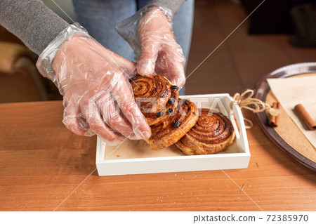 Hands in transparent gloves put buns in a box 72385970