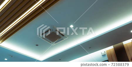 Selective focus on cassette type air conditioner mounted on ceiling wall. Air duct on ceiling in hotel. Air heading unit on gypsum wall. Cool system in the building. Air flow and ventilation system. 72388379
