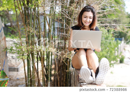 attractive freelance asian woman in black casual shirt, short hairs and short jean working with computer laptop on sandy beach during sunny day with happy smiling face attractive freelance asian woman in black casual shirt, short hairs and short jean working with computer laptop on sandy beach during sunny day with happy smiling face 72388986