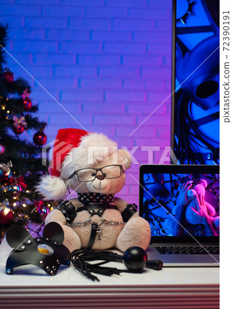 a Teddy bear in a leather belt an accessory for BDSM games in a Santa Claus hat next to a laptop a neon TV and a Christmas tree a Teddy bear in a leather belt an accessory for BDSM games in a Santa Claus hat next to a laptop a neon TV and a Christmas tree 72390191