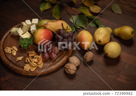 Angle view. Wine snacks set: selection of cheese, grapes, pear and three walnuts on a wooden table. Brie cheese with fruits, grapes, walnuts on a dark wooden plate and wooden board 72390982