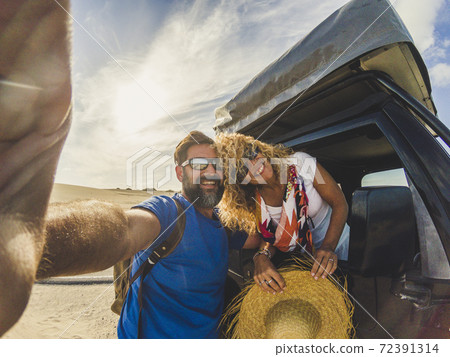 Cheerful beautiful youth adult caucasian couple enjoy and take a slefie picture with them and the car with tent on the roof - alternative vehicle for vacation and happy people together free 72391314