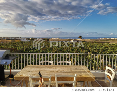 Beautiful view of wooden table and barbecue kitchen grill ready to host people to have un together - nature and home concept - blue sky and ocean in background Beautiful view of wooden table and barbecue kitchen grill ready to host people to have un together - nature and home concept - blue sky and ocean in background 72391423