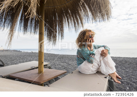 Happy cheerful caucasian woman do a phone call sitting on a sunbed at thebeach during summer trendy holiday vacation at the beach - travel and technology people concept Happy cheerful caucasian woman do a phone call sitting on a sunbed at thebeach during summer trendy holiday vacation at the beach - travel and technology people concept 72391426