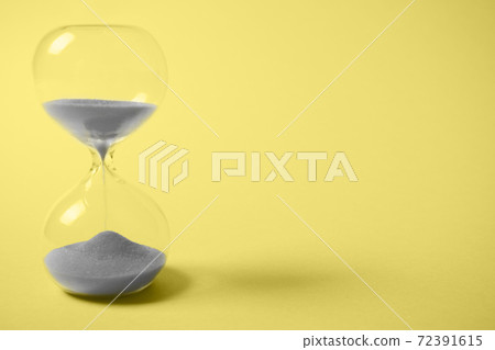 Hourglass with gray sand on yellow background. 72391615