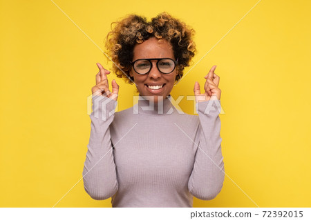 Cheerful African American woman awaits for miracle, prays and hopes dreams come true, crosses fingers for good luck Cheerful African American woman awaits for miracle, prays and hopes dreams come true, crosses fingers for good luck 72392015