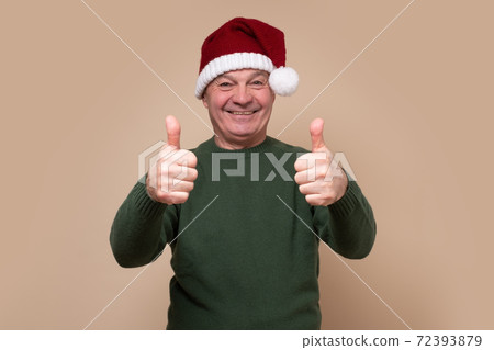 Senior man wearing santa claus hat doing happy thumbs up gesture with hand Senior man wearing santa claus hat doing happy thumbs up gesture with hand 72393879