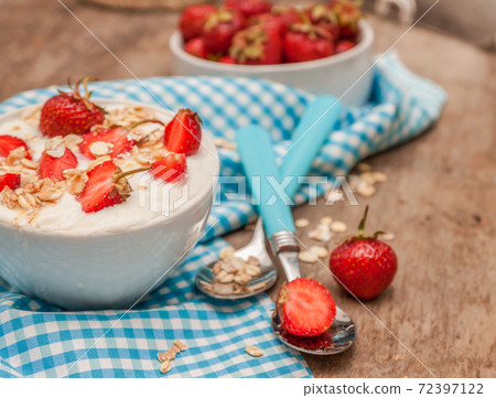 In a cup of yogurt, oat granola and fresh strawberries, on a blue spoon towel, scattered oatmeal and 72397122