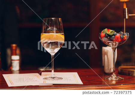Cocktail with lemon in glass on bar desk with menu Cocktail with lemon in glass on bar desk with menu 72397375